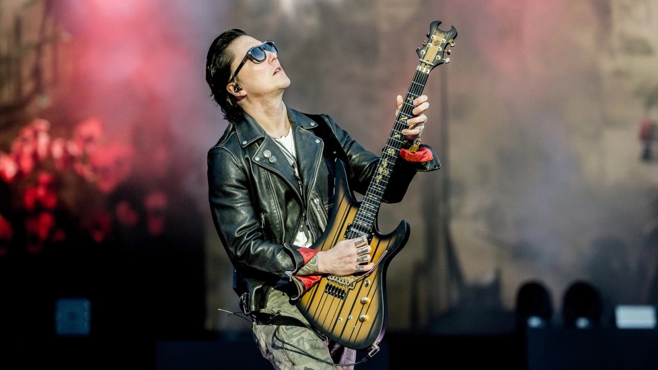 Synyster Gates playing guitar live on stage.